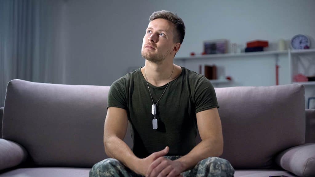 Soldier in military green and dog tags sits on a couch looking up hopefully