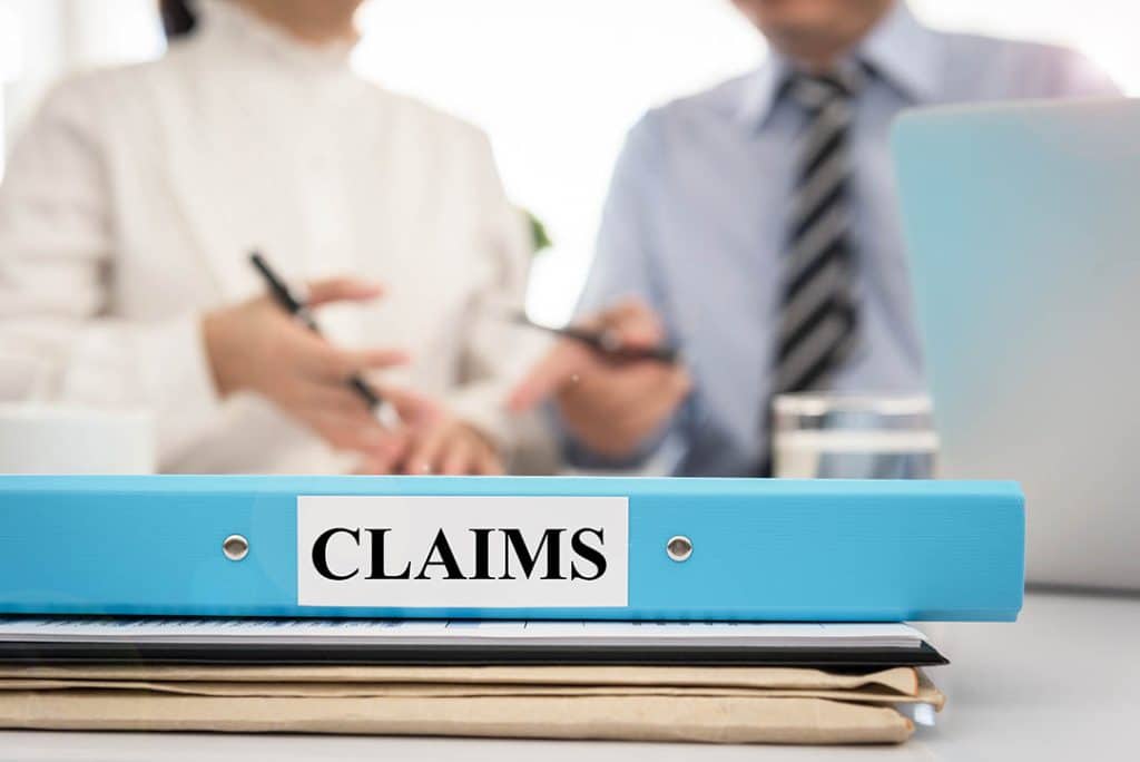 Folder marked "claims" in the foreground with two professionals discussing a business matter in the background