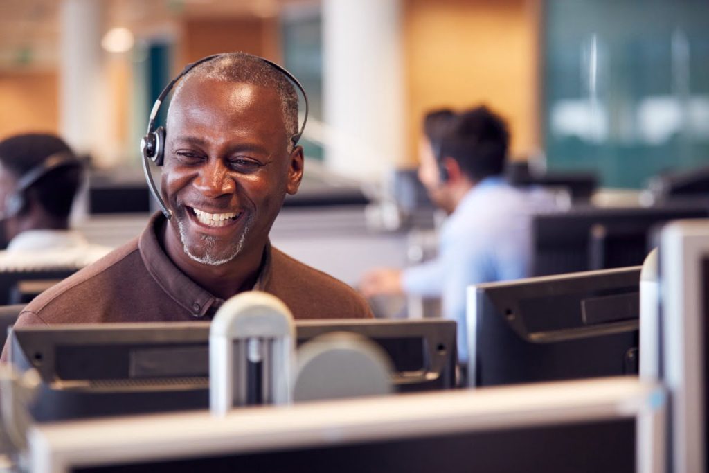 mature man sitting at computer with a headset on.